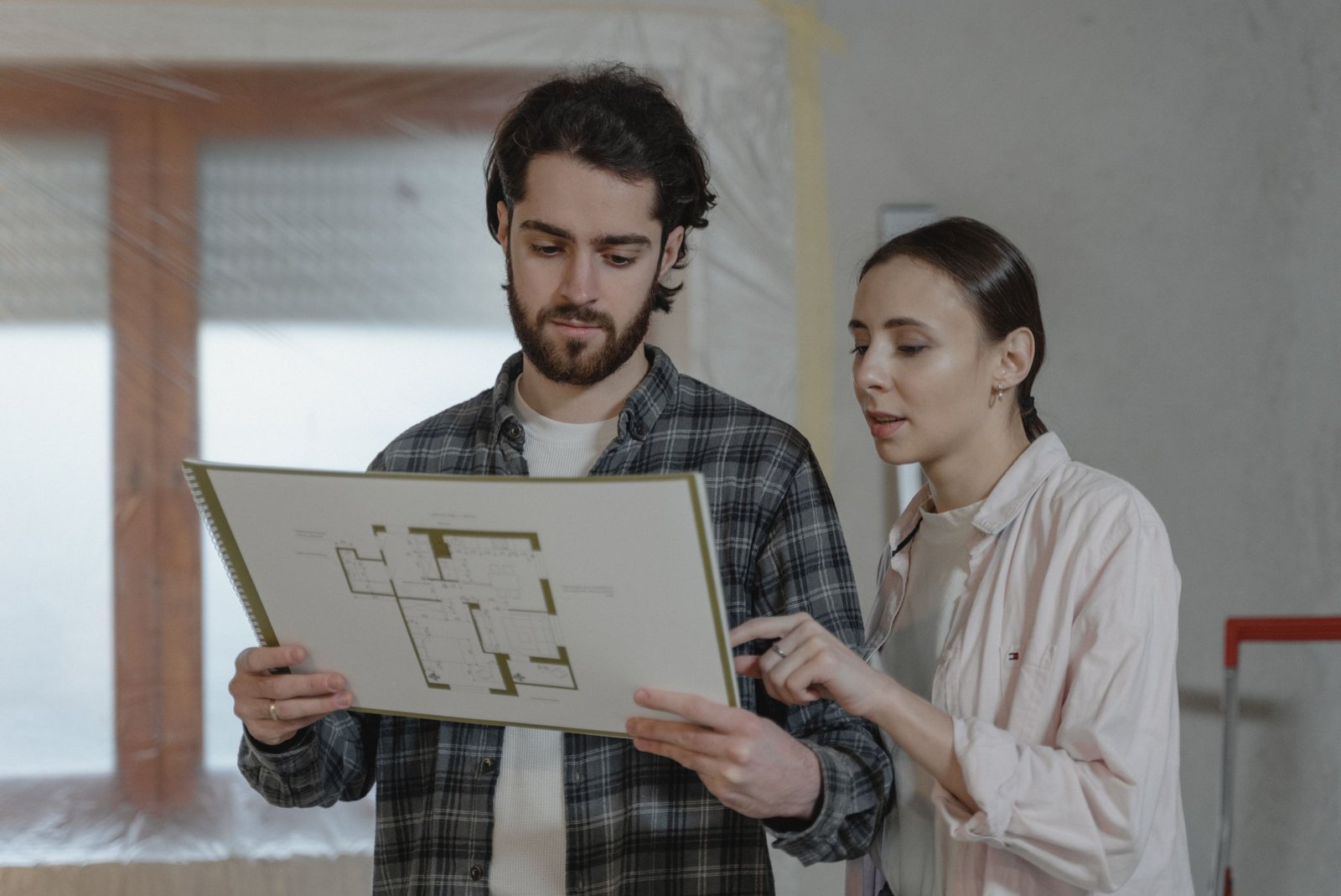 Un artisan et un couple examinent un devis de travaux sur une tablette dans un salon en rénovation.