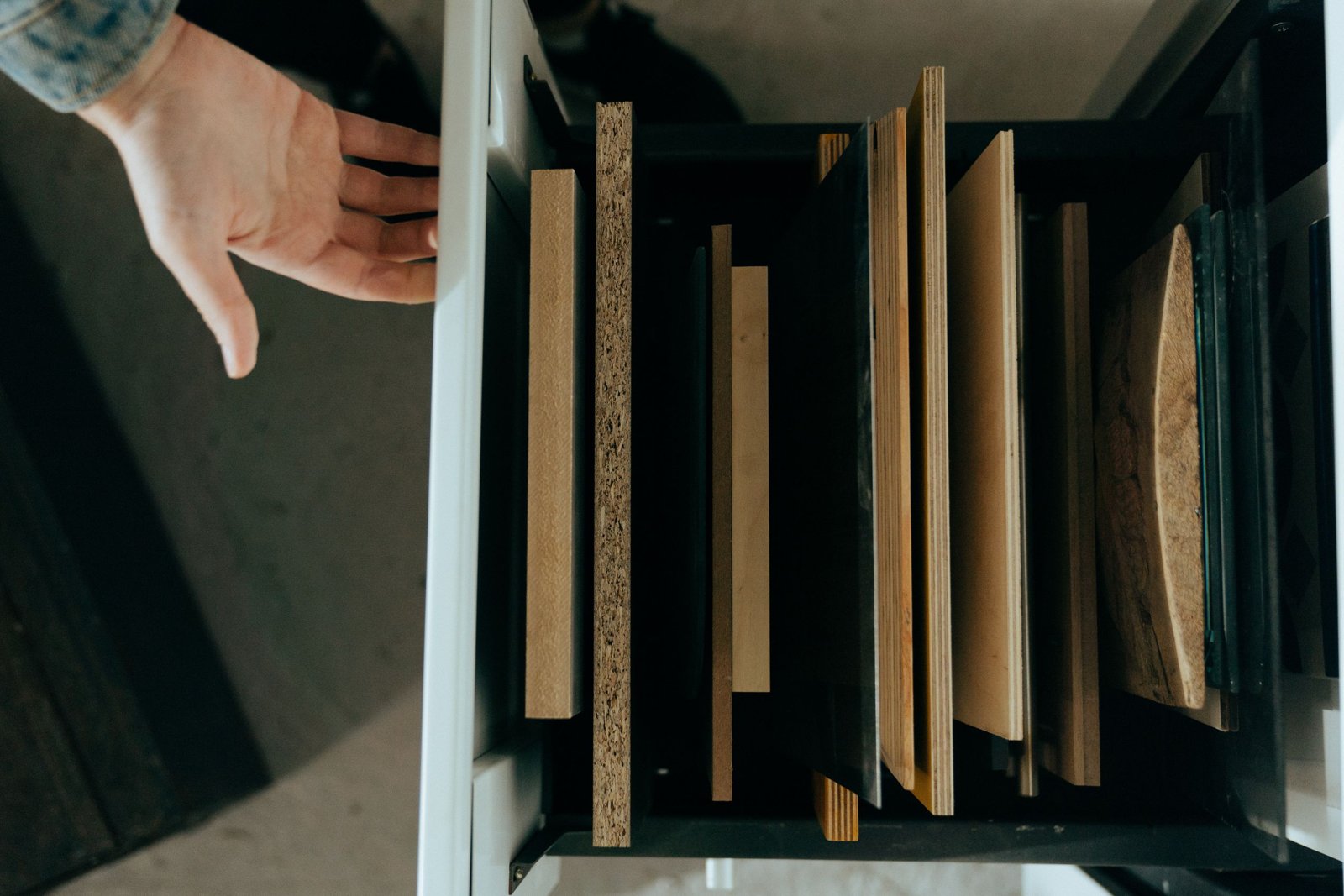 Gros plan sur une feuille de placage bois enroulée, veinage chaud, atelier lumineux et outils de découpe.